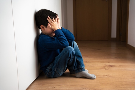 Sad child with head in hands sitting on floor