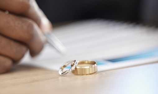person signing divorce papers with wedding rings in the foreground